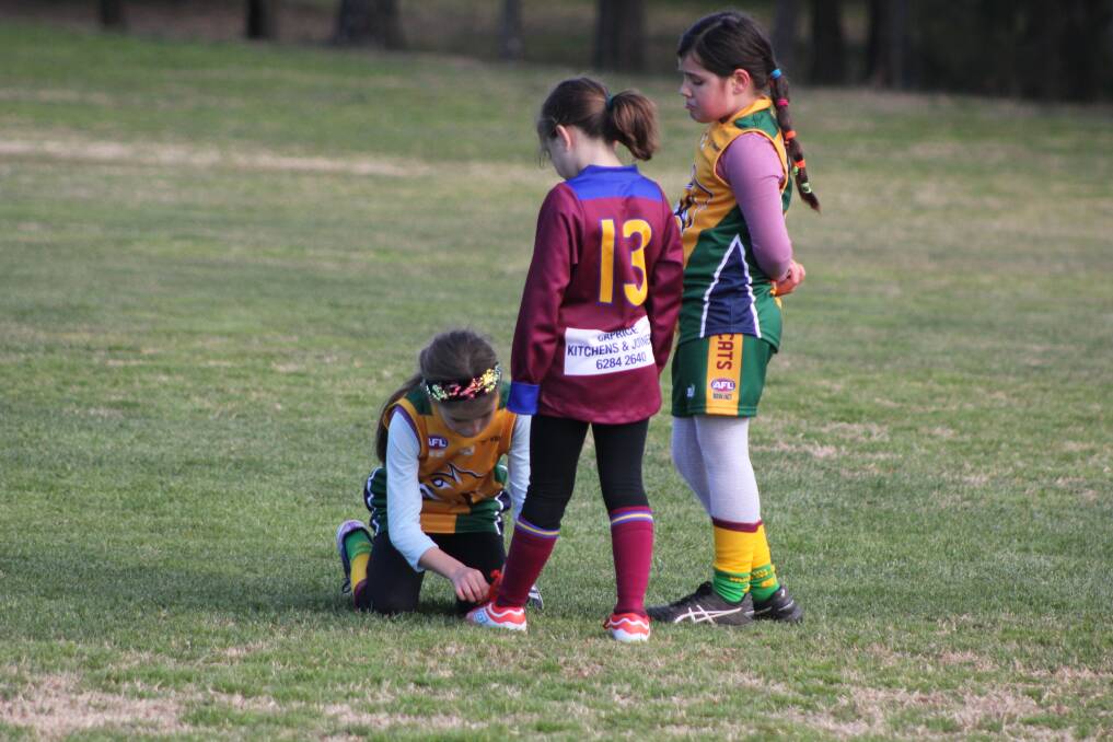 Luke Hickey's photograph at the under 10s girls AFL game as Weston Creek Molonglo Wildcats player Gemma Klose ties the shoelace of an opposition player, Tuggeranong Lions' Lily Tompkins. Picture: Luke Hickey