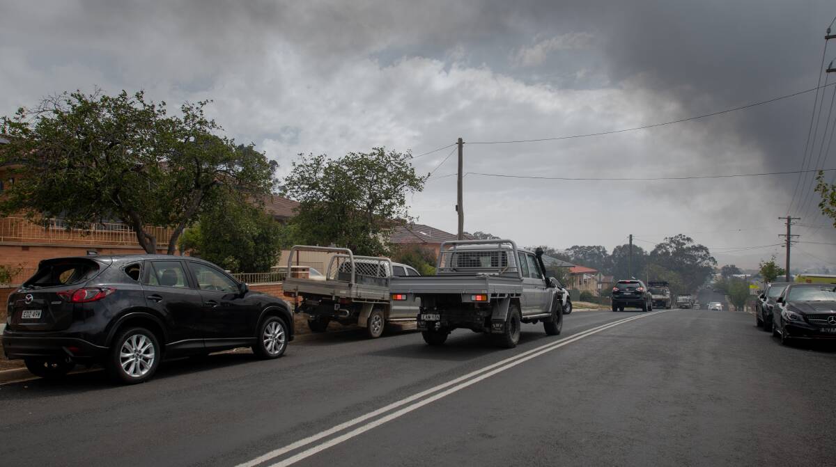 Damaged cars during the Canberra hailstorm as smoke rises from nearby fires. Picture: Elesa Kurtz