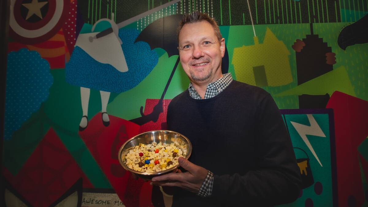 Limelight Cinema owner Ross Entwistle with the loaded popcorn in front of the new mural featuring movies from Harry Potter to Back to the Future. Picture: Karleen Minney