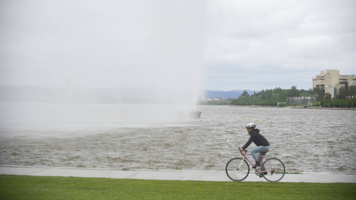 A cyclist rides past the Captain Cook jet on Lake Burley Griffin, as wet and windy conditions persist. Picture: Dion Georgopoulos