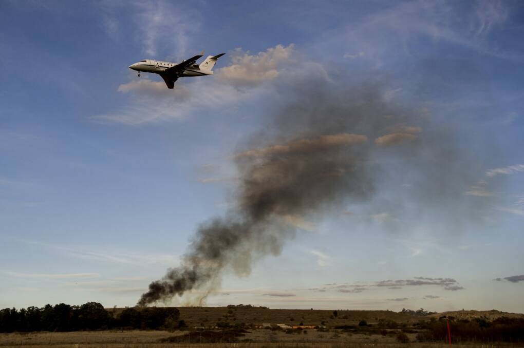 A plane flies over the fire near Canberra Concrete Recyclers on Pialligo Avenue. Photo: Jay Cronan