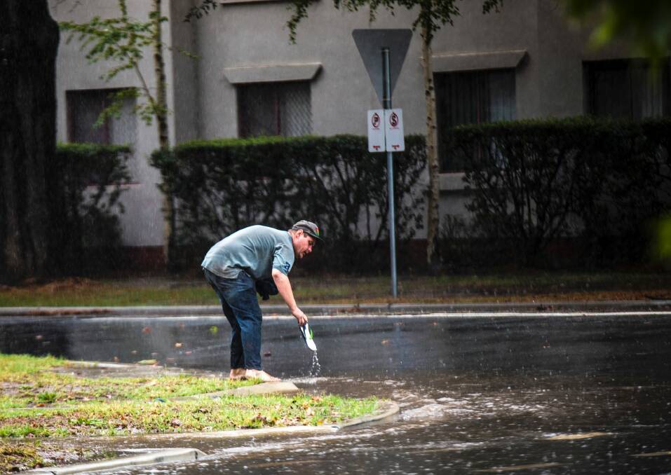 A man retrieves a thong after losing it on a waterlogged Kingston street on Tuesday. Photo: Sitthixay Ditthavong