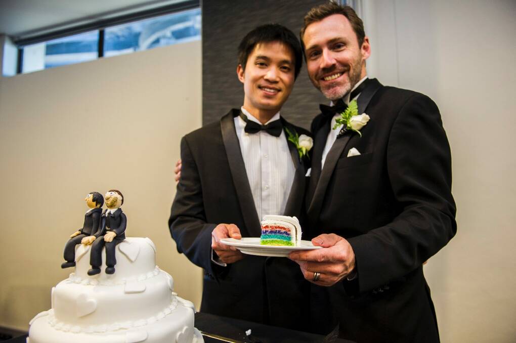 Ivan and Chris Hinton-Teoh hold a slice of their rainbow wedding cake from Erindale Bakery next to the cake toppers made by Nada's Cakes.  Photo: Rohan Thomson