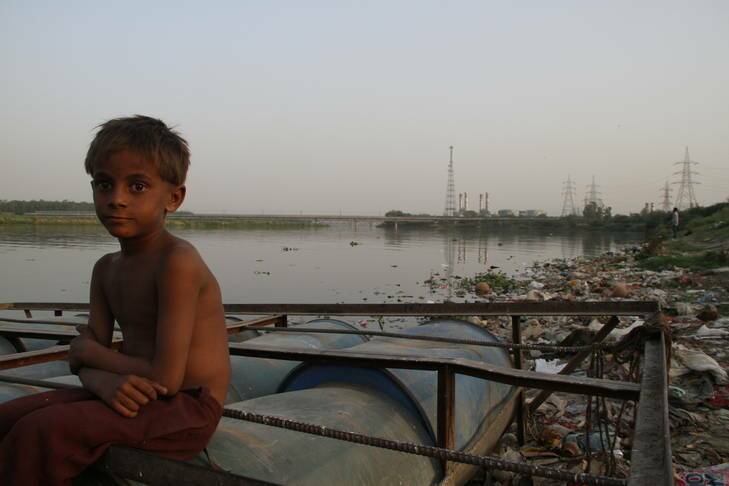 Amid the foul stench of the riverbank, a young "ragpicker" sits near the detritus of one of India's most polluted waterways. Photo: Ben Doherty