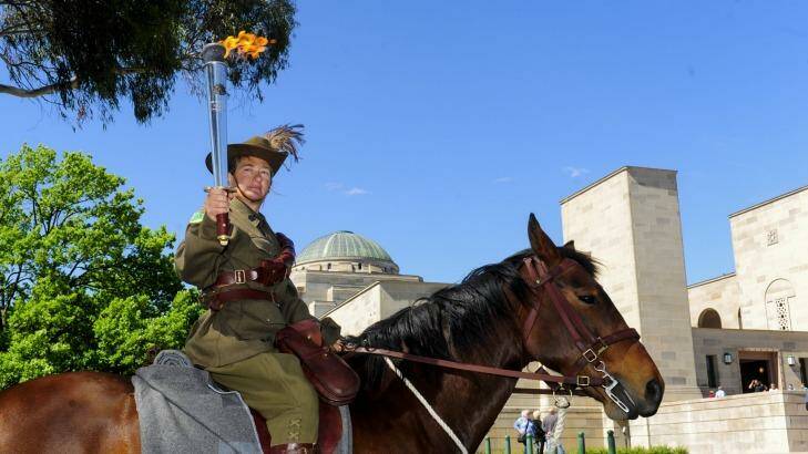 FIRE AND ICE: Jennifer Cayfe, in the full uniform of one of the Light Horse regiments, holds the Anzac Flame aloft as Comet keeps his cool amid  the fuss. Photo: Melissa Adams 
