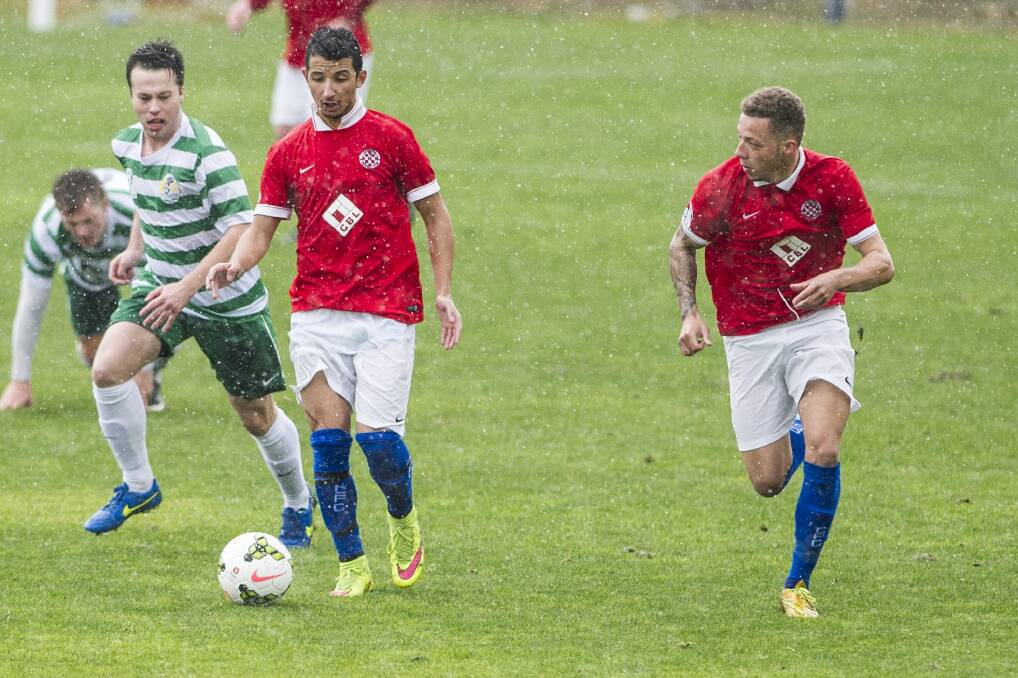 Canberra FC players Thomas James, right, and Muad Zwed, middle, in action as the rain comes down on Sunday afternoon. Photo: Jay Cronan