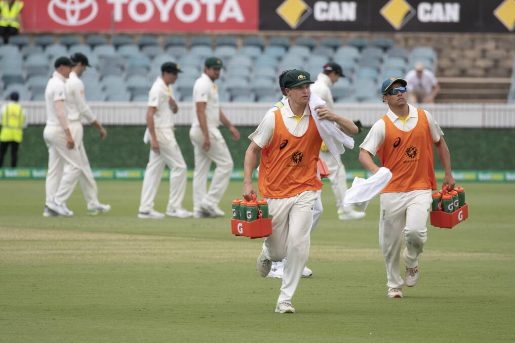 Substitute fielders Tom Vane-Tempest and Dan Leerdam run drinks out to the Australian cricket team. Photo: Sitthixay Ditthavong