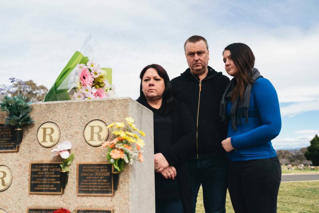 Mark Knowles, with his wife Tracy and daughter Ashley, visit the plaques at Queanbyean Lawn Cemetery for his mother, Carol Saxton, and his sister, Patricia Riggs. Photo: Rohan Thomson