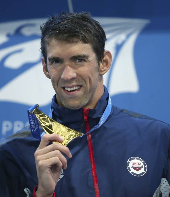 Michael Phelps holds up his men's 100m butterfly gold medal at the Pan Pacific Swimming Championships held on the Gold Coast in August. Photo: AP