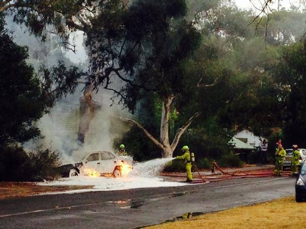 Firefighters battle to put out a car fire on Dryandra St, O'Connor. The car was struck by lightning, and is also above an underground gas leak. Photo: Sarah Groube