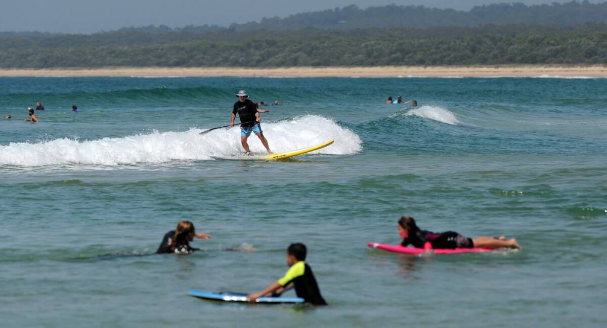 A stand up paddle boarder catches a wave at south Broulee Beach this summer.  Photo: Graham Tidy