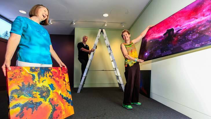 Capturing the Cosmos opens at the CSIRO Discovery Centre February 1st. Cris Kennedy of CSIRO Discovery helps artists Jacquie Roger (left) and Arlene Williams hang their work. Photo: Katherine Griffiths
