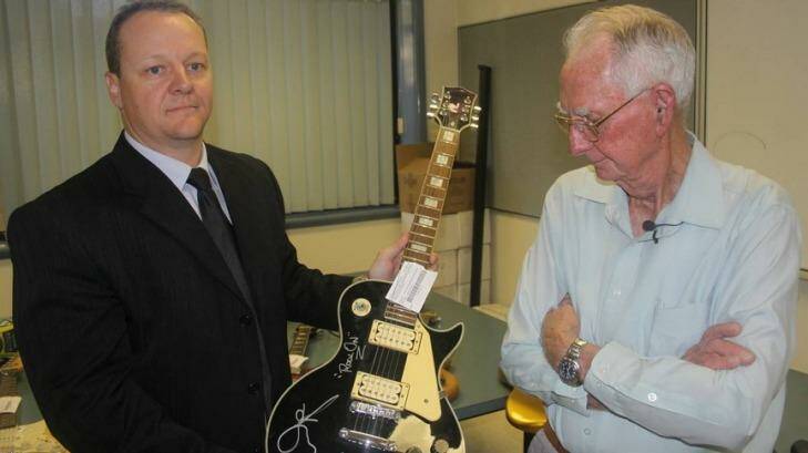 Detective Senior Constable Lonie Horn holds up one of the recovered guitars as its owner, Leonard "Merv" French, looks on. Photo: Stephen Jeffery