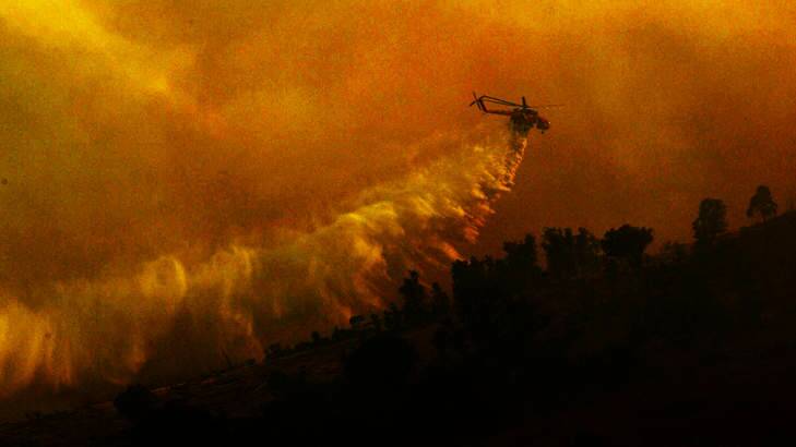 A helicopter water bombs a pine plantation near the Brindabellas during the 2003 Canberra bushfires. Photo: Nick Moir