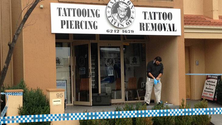 UNDER FIRE: An investigator at the Tatts On Tatts Off tattoo parlour where bullet holes were discovered in the shop front on Tuesday morning. Photo: Matthew Raggatt