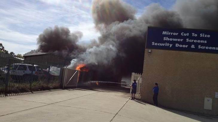 Neighbours hose down the boundary of their property as a fire burns at a Mitchell car yard. Photo: Ewan Gilbert (via Twitter @ewangilbert)