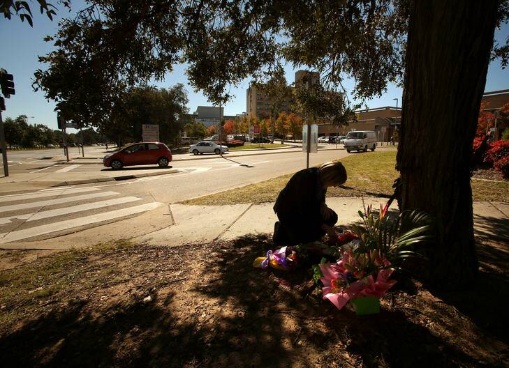 A hospital worker looks at flowers that are left at the scene of an accident outside The Canberra Hospital. Photo: Penny Bradfield