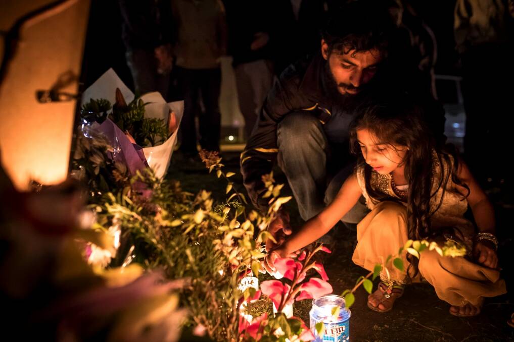 Adnan Amjid, friend and housemate of Zeeshan Akbar, helps a girl light a candle at a vigil. Photo: Sitthixay Ditthavong