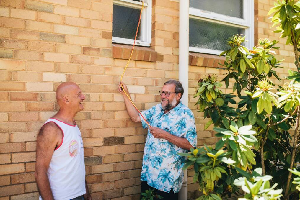 Axel Godeck with his neighbour Jim Croft at home in Campbell. Croft hasn't had power since Friday when a tree damaged the power lines outside his home so Godeck ran a power lead from his home so that Croft could charge his phone. Photo: Rohan Thomson
