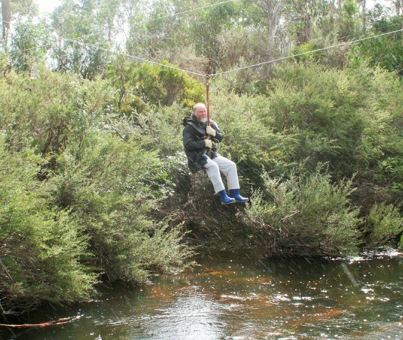 Constructed 35 years ago by his neighbour, Wolf Heyer crosses the flooded Tuross River on a home-made flying fox. Photo: Wolf Heyer