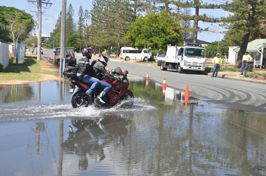Motorbike riders travel through saltwater flooding in Scarborough, north of Brisbane.