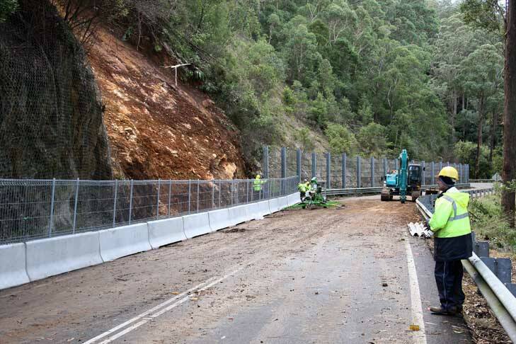Race to reopen ... workers fix fencing following the landslide on the Kings Highway. Photo: Jeffrey Chan