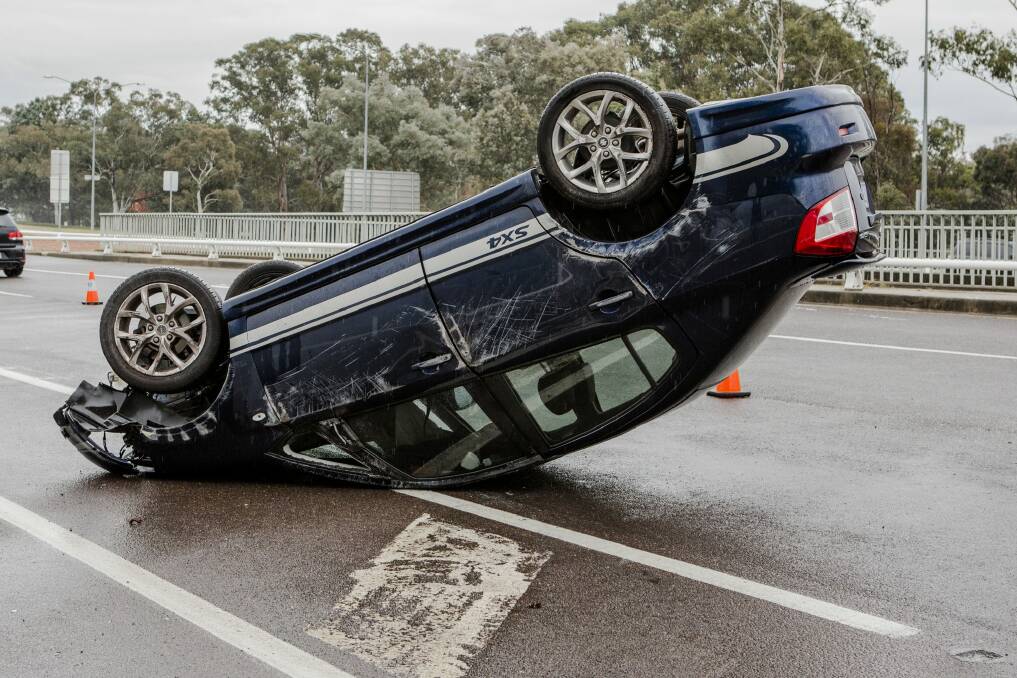 A car landed on its roof on Adelaide Avenue on Saturday morning as wet weather continued to affect the capital. Photo: Jamila Toderas 