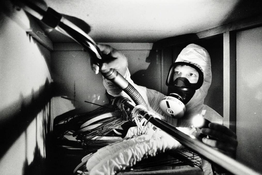 Dmark Giersch with his protective gear on crawls into a cupboard of a house in Campbell to vacuum away dust and asbestos that may have leaked into the house from the roof through cracks at the top of built in robes. From the original removal program. Photo: Canberra Times