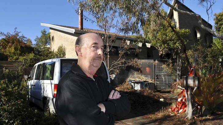 A neglected and unfinished home in Yambina Crescent, Warramanga, much to the ire of immediate neighbour, Wayne Mitchell, pictured in front of the house. Photo: Graham Tidy