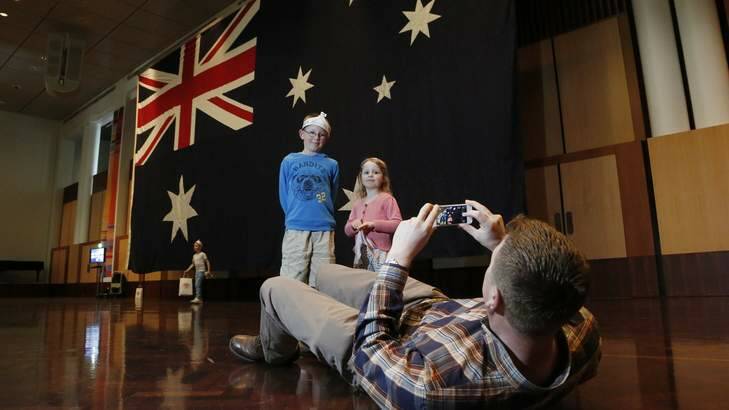 Jason Corbett- Jones from Griffith, right, takes a photo of Callum Corbett- Jones 8, left, and Chloe Corbett- Jones 3, centre, in front of the Parliament House Flag in the Great Hall during the Parliament House 25th Anniversary Open Day. Photo: Jeffrey Chan