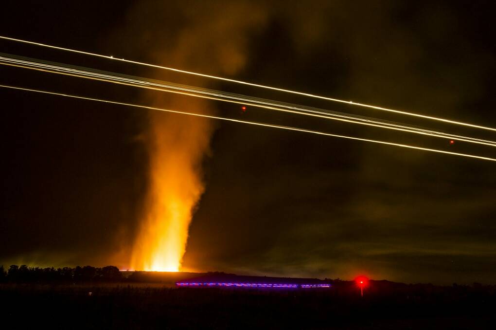 Planes continue to land  while a fire near the Canberra Concrete Recyclers on Pialligo Avenue blazes away on Thursday night. Photo: Jay Cronan