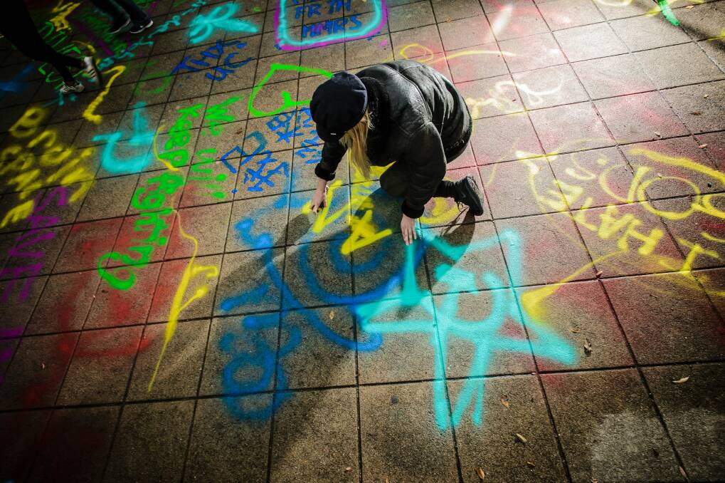 ANU student Skye Jamieson spraypaints a message on Union Court. Photo: Sitthixay Ditthavong