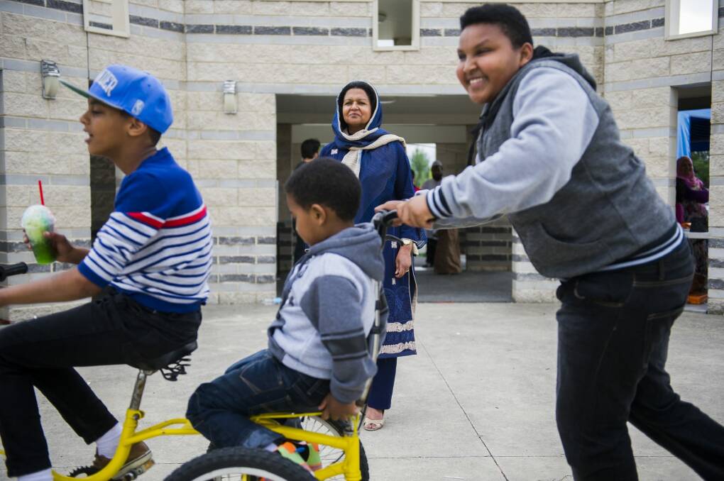 Boudi Yasir, 11, Muayed Hamed, 6, and Muhayed Hamed, 13, play on a bike in front of Canberra Islamic Centre president Azra Khan at the Mosque Open Day on Saturday. Photo: Rohan Thomson
