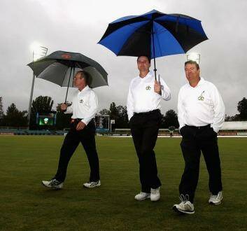 The umpires walk off Manuka Oval after inspecting the pitch during Monday's rain delay.