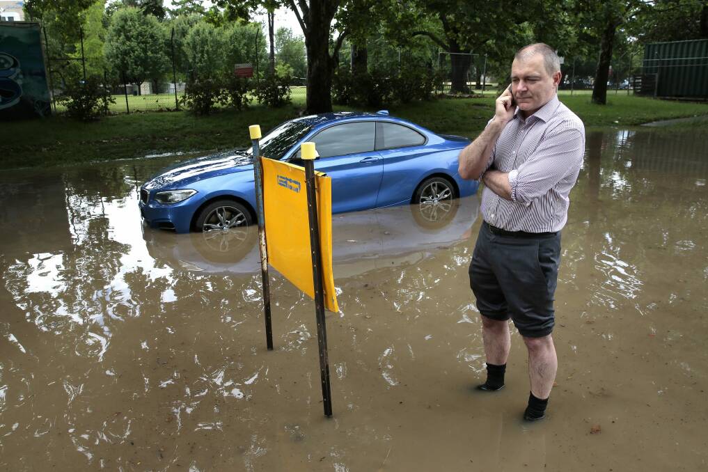 Michael Rorke on the phone to his insurance company after becoming stuck in a flooded part of the parking lot at Canberra Olympic Pool. Photo: Jeffrey Chan