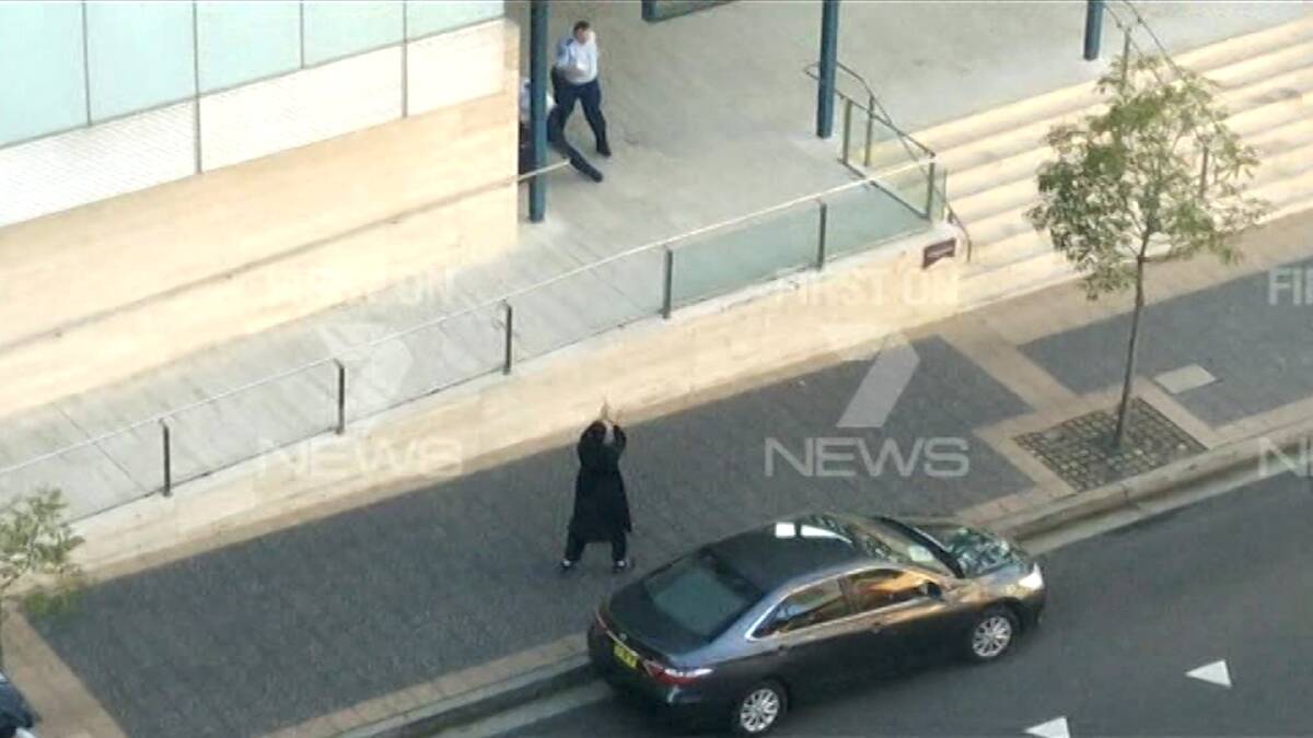 Farhad Khalil Mohammad Jabar, dressed in black, points his gun outside the Parramatta police station. Photo: Channel Seven