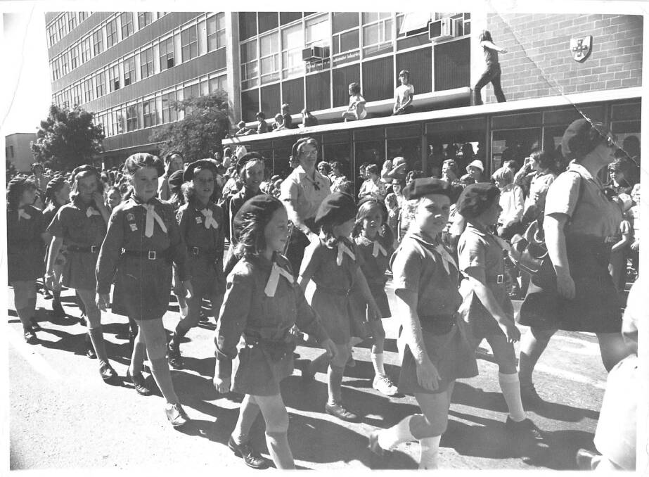 A parade of Guides and Brownies in Canberra in 1964. Note the casual OH and S vibe at the time as kids scramble on to rooftops to watch the passing parade.  Photo: Supplied
