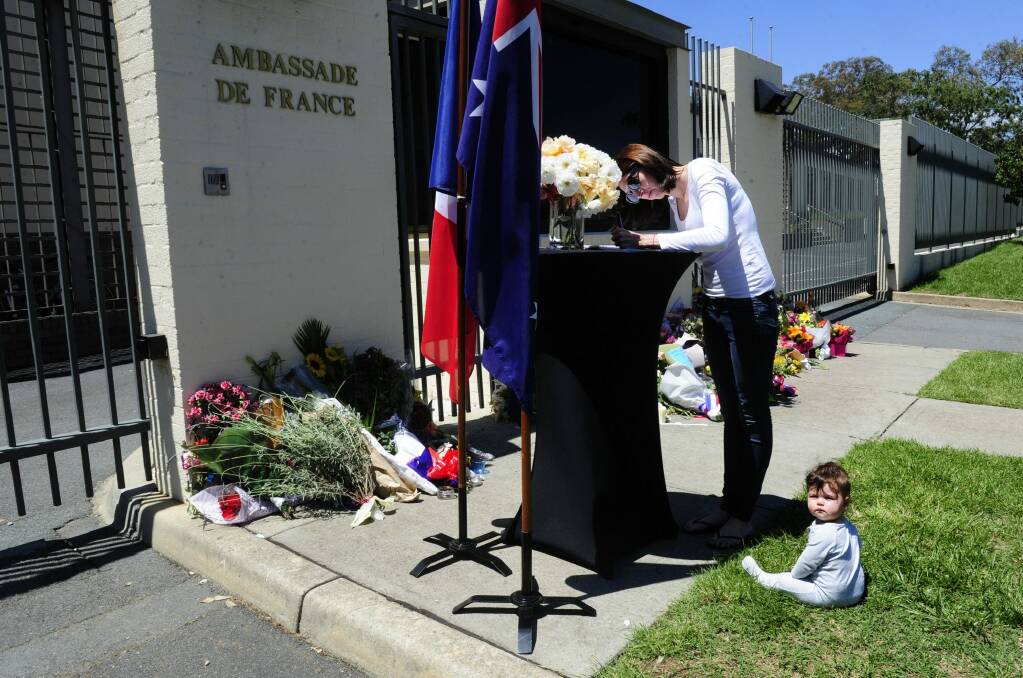 Kamara Buchanan, of Fisher, with her daughter Sophie, seven months, writes a message in a condolence book outside the embassy of France.  Photo: Melissa Adams 
