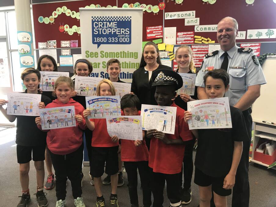 Crime Stoppers ACT region chair Diana Forester and ACT Policing Acting Superintendent Jason Kennedy with North Ainslie Primary School children, who are showing off their Crime Stoppers Week colouring in competition entries.  Photo: Supplied