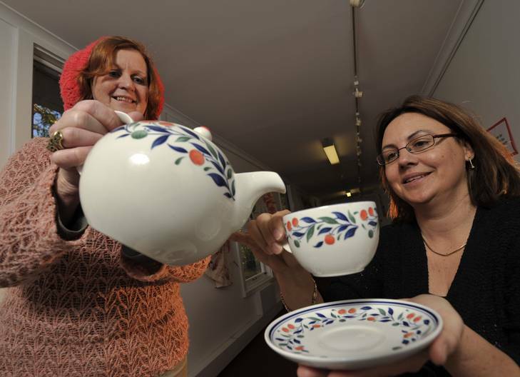 Assistant executive director of Southside Community Gallery Libby Mills served tea by Lyn Diskon with the latest exhibition collection of teapots and tablecloths. Photo: Jay Cronan