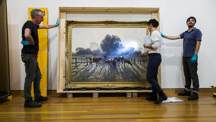 <em>Spring Frost</em> by Elioth Gruner is hung at the Canberra Museum and Gallery while Melissa Harvey inspects the work for any damage. Photo: Rohan Thomson