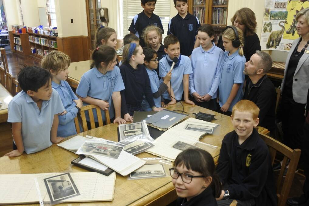 Ainslie School year 6 students Nicole Domigan and Ben Francis look at archival photos as their classmates record interviews as part of 90th anniversary celebrations. Photo: Stephen Jeffery