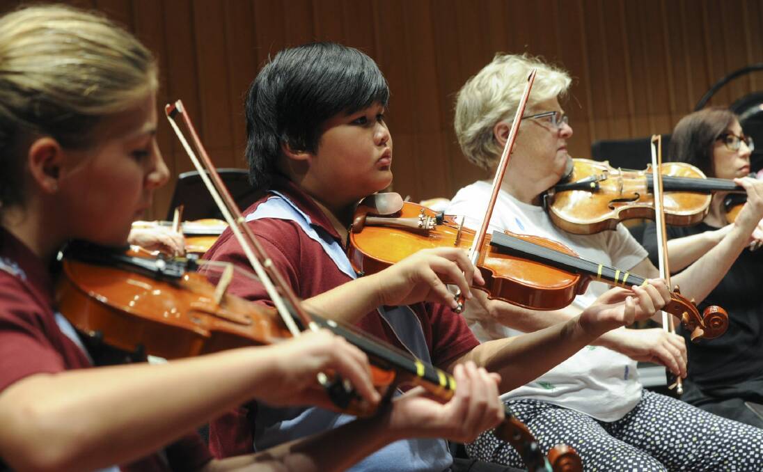 Goulburn Public School year five pupils Teesha Jones, left, and Brendell Guiao sit next to CSO first violinist Barbara Jane Gilby at a rehearsal for Tuesday's performance. Photo: Graham Tidy