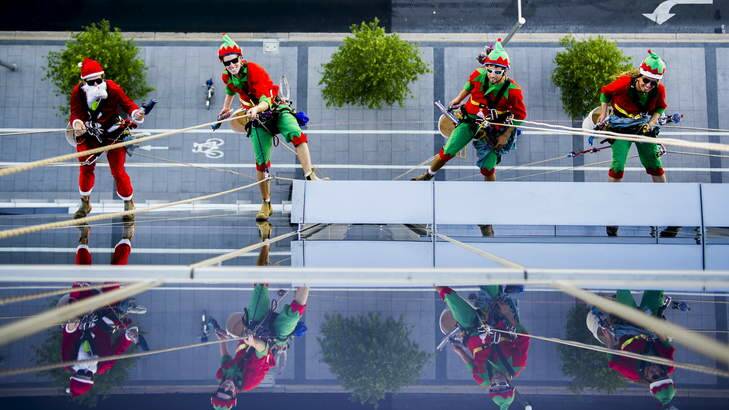 Touchdown's Mitch Lawry, Michael Eland, Lincon Bart, and Laurie Coughlen clean the windows of 50 Marcus Clarke Street, dressed as Santa and his Elves. Photo: Rohan Thomson