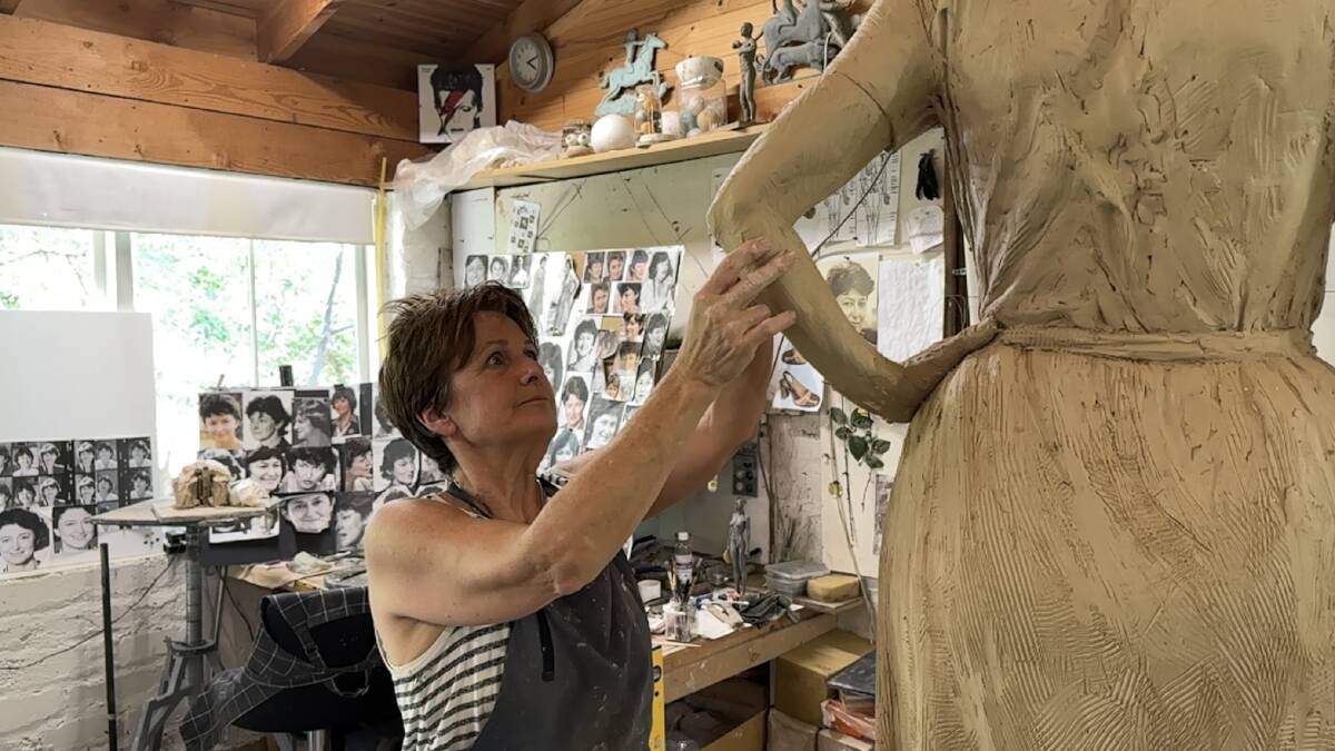 Artist Lis Johnson works on a sculpture of Susan Ryan in her studio in Victoria, with pictures of the late senator on the wall behind her. Picture supplied