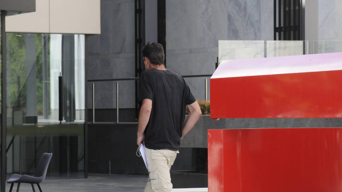 Ryan Harder turns his back on media and goes to hide behind a sculpture outside the ACT Magistrates Court following his release on bail. Picture: Blake Foden