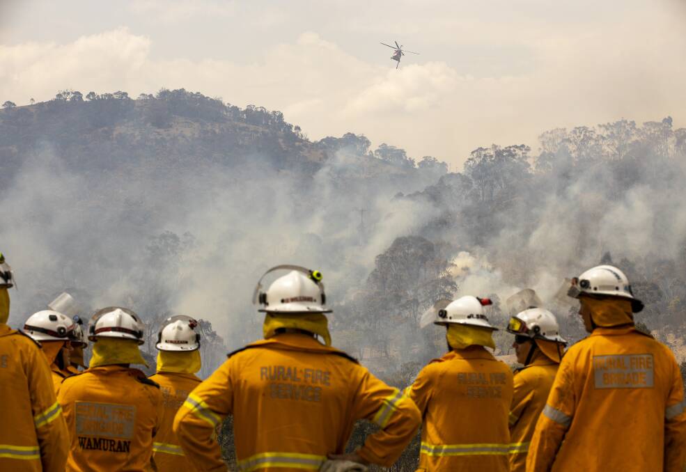Fire crews watch as a helicopter is used to fight a fire threatening a property on Boboyan Road during the 2020 Orroral Valley fire. Picture: Sitthixay Ditthavong