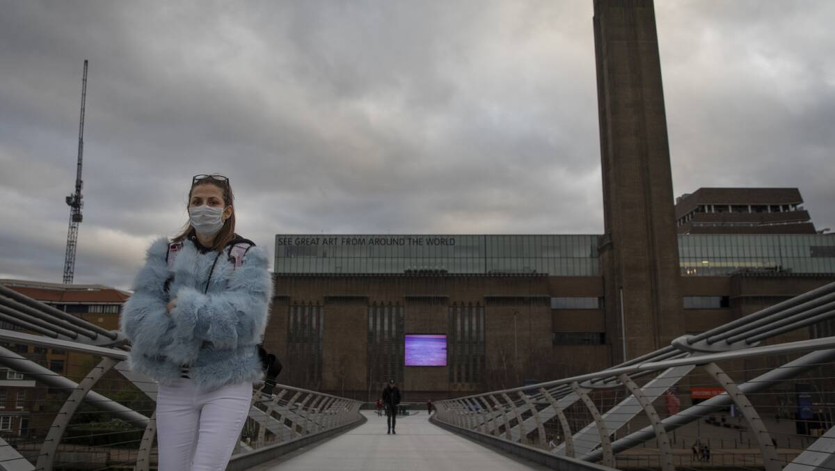 A woman wearing a face mask walks over Millennium Bridge near the Tate Modern in London, which has closed its doors amid the coronavirus outbreak. Picture: Getty Images. 