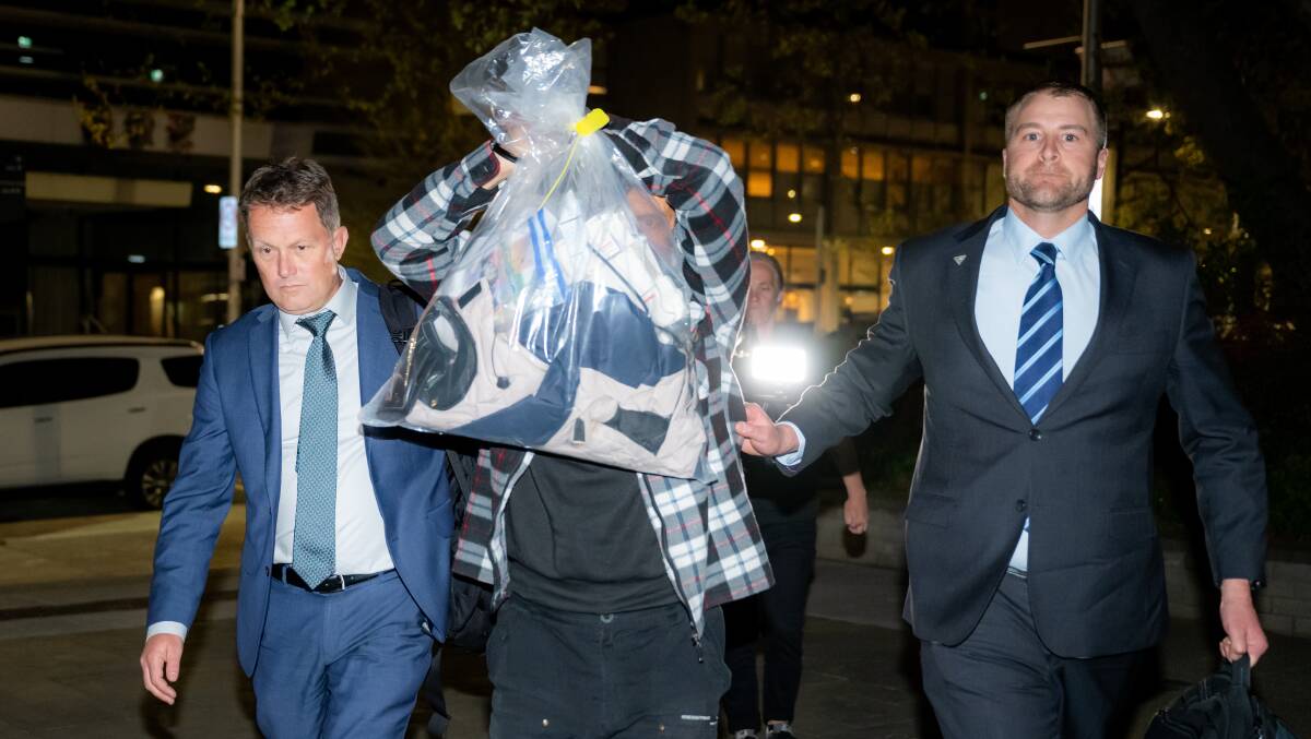 Steve Fabriczy holds up a bundle of clothes in an attempt to shield his identity as he is led into Canberra City police station last month. Picture by Elesa Kurtz