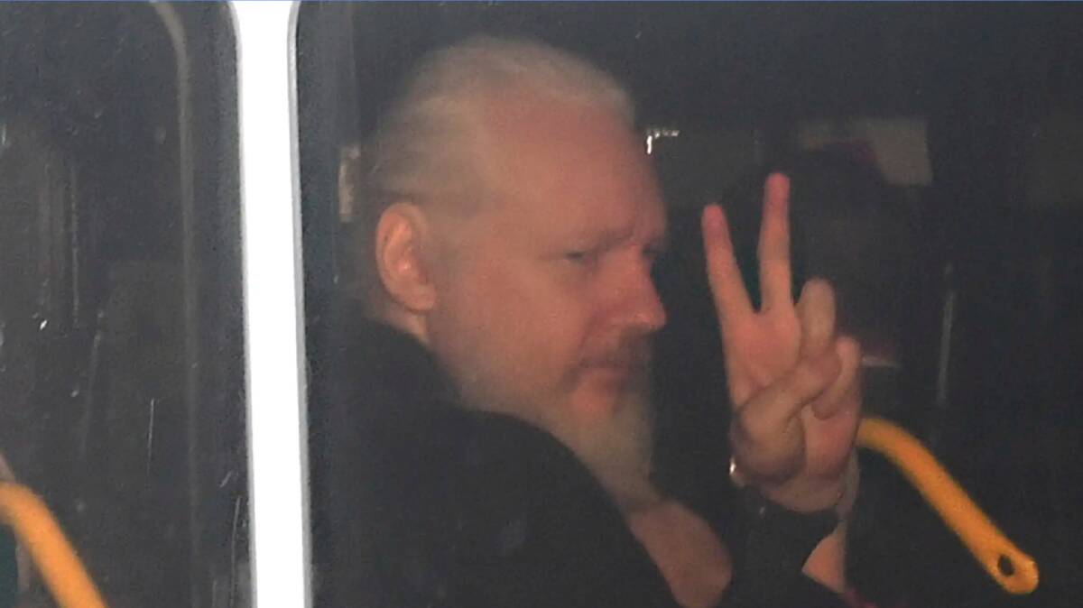 Julian Assange signals to media from the police van after his arrest. 